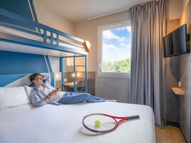 A hotel room with a bunk bed, a desk, a chair, a TV, and a tennis racket on the bed.