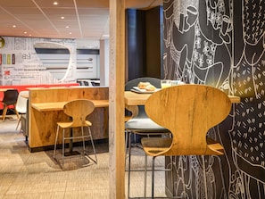 A modern cafe interior with wooden furniture, a chalkboard wall with drawings, and a visible menu board.