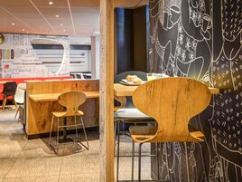 Interior de una cafetería moderna con muebles de madera, una pared de pizarra con dibujos y un cartel de menú visible.