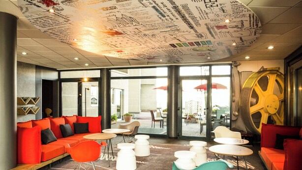 Een moderne zithoek met een rode bank, witte tafels en een uniek plafondontwerp.