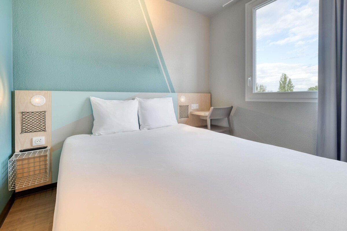 A hotel room with a bed, bedside tables, a chair, a window, and a view of the sky.