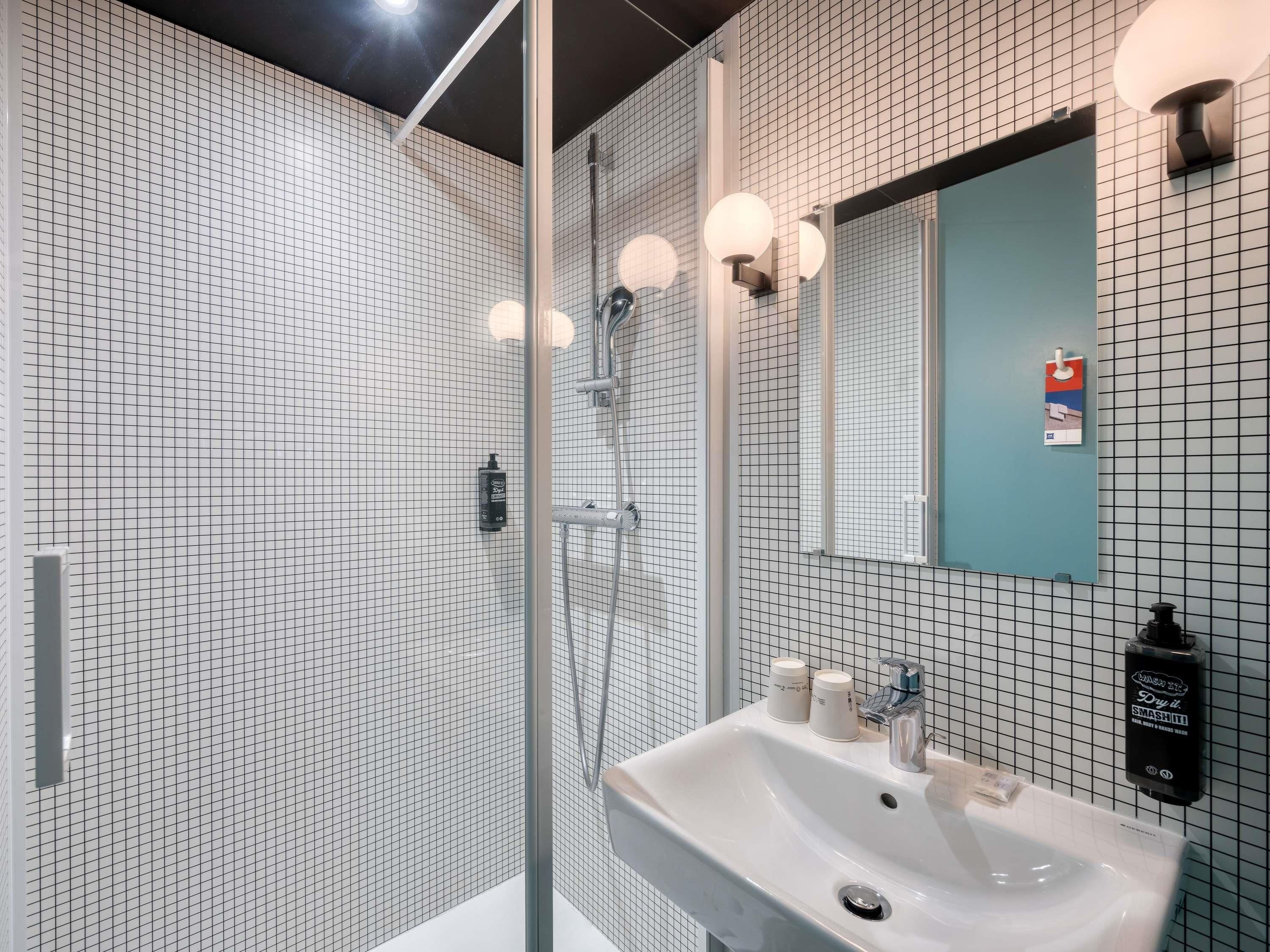 Een moderne badkamer met een douchecabine van glas, een wastafel met spiegel en betegelde wanden.
