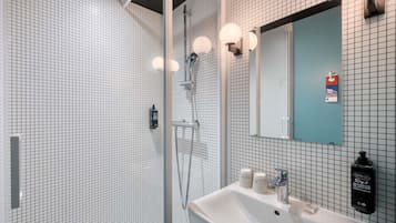 Ein modernes Badezimmer mit einer gläsernen Duschkabine, einem Waschbecken mit Spiegel und gefliesten Wänden.