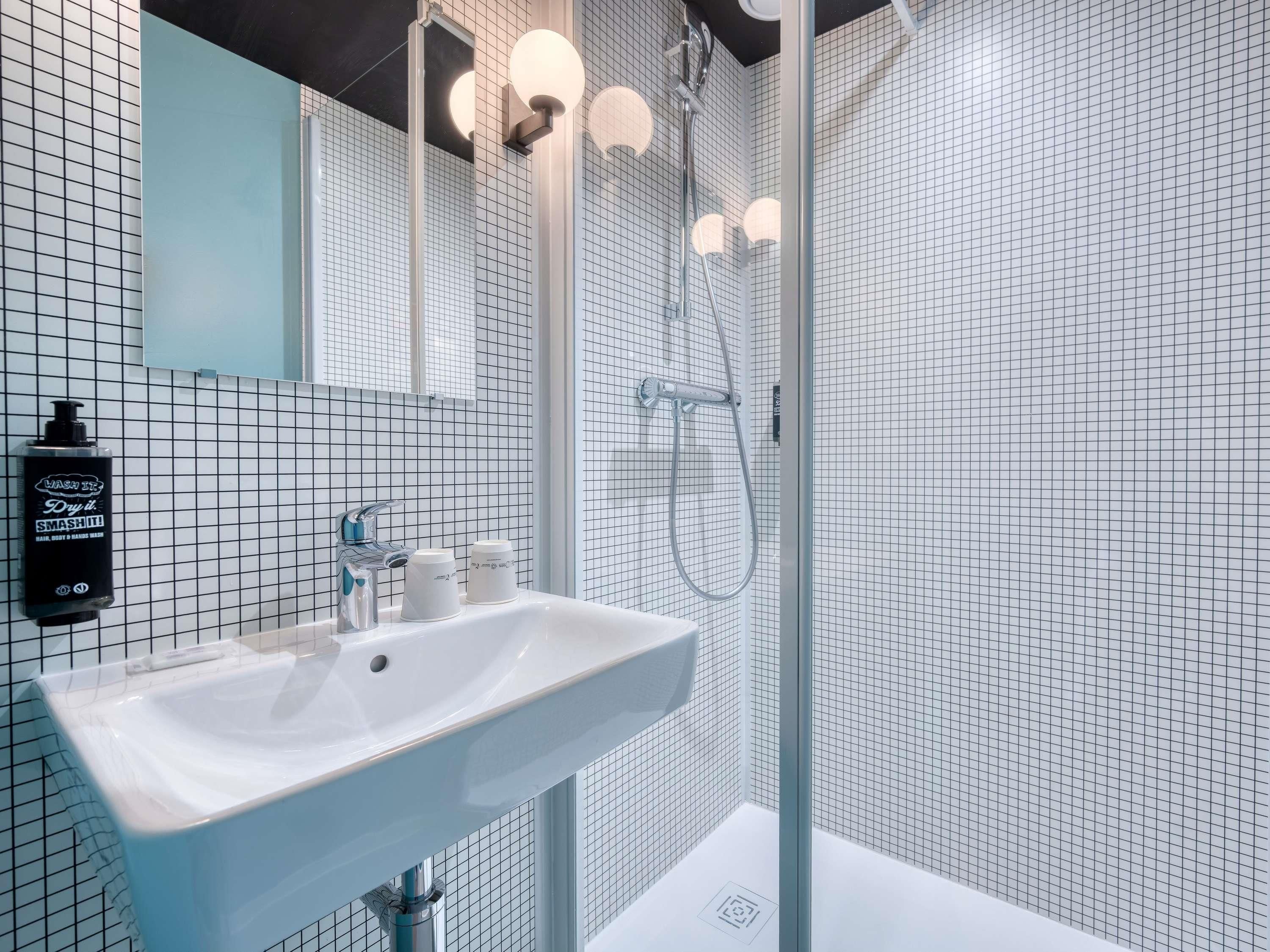 A modern bathroom with a white sink, a handheld showerhead, and a mirror with lights.