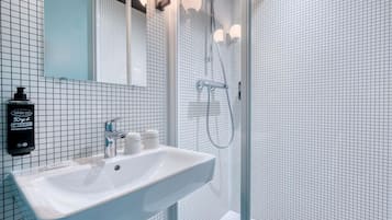 A modern bathroom with a white sink, a handheld showerhead, and a mirror with lights.