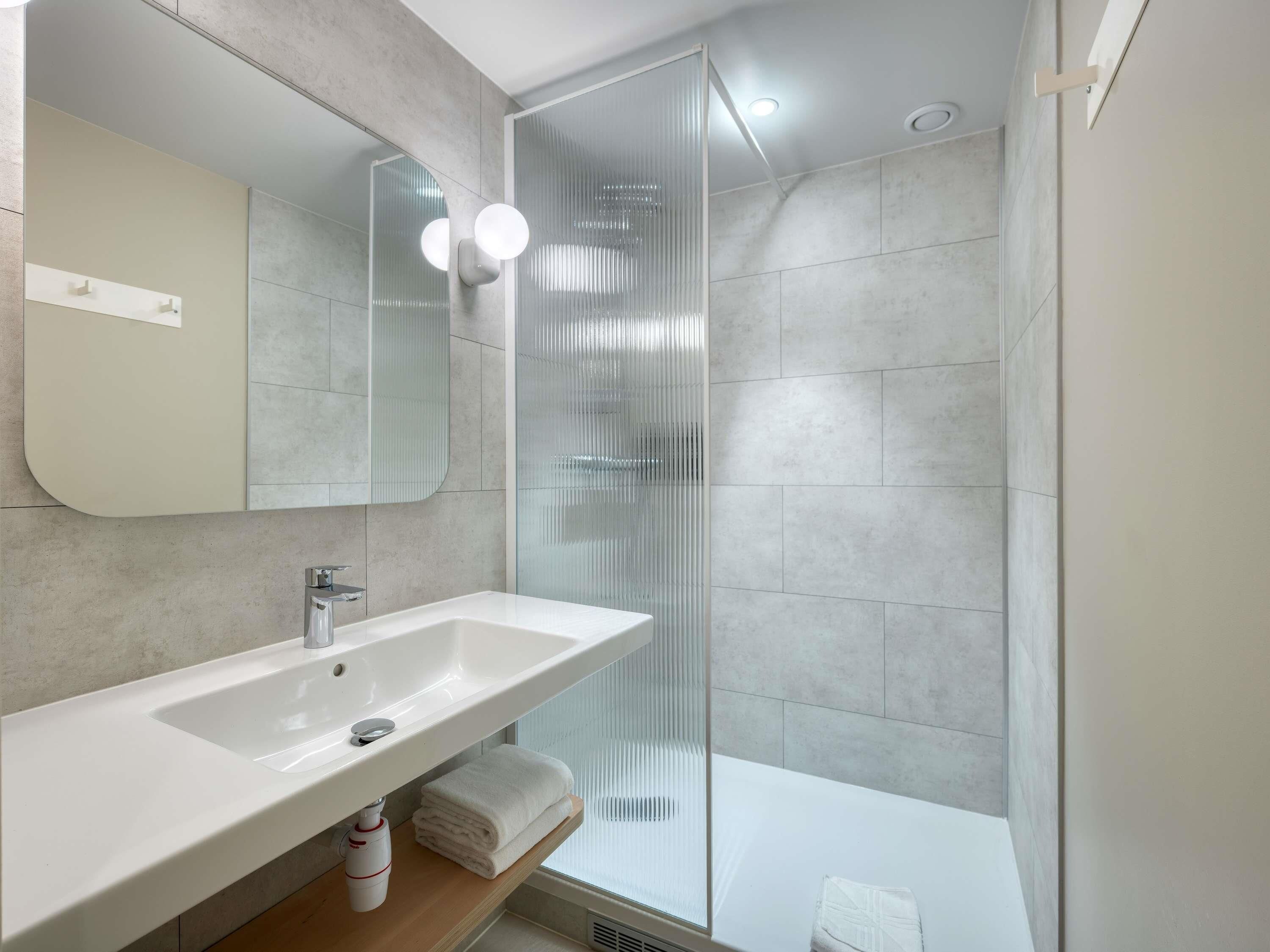 A modern bathroom with a large mirror, a sink, and a glass shower enclosure.