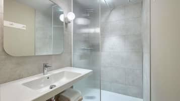 A modern bathroom with a large mirror, a sink, and a glass shower enclosure.