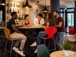 A bar area with a counter, stools, and a variety of bottles on shelves.