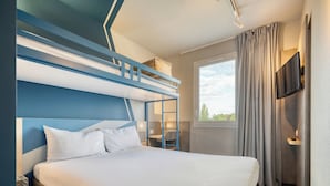 A modern hotel room with a bunk bed, a flat-screen TV mounted on the wall, a window with curtains, and a bedside table. - ibis budget Orly Chevilly Tram 7 (Chevilly-Larue)
