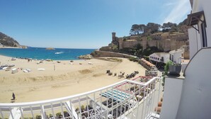 A beach with a castle on a hill, a pool area, and a view of the sea. - Hostal del Mar (Tossa de Mar)