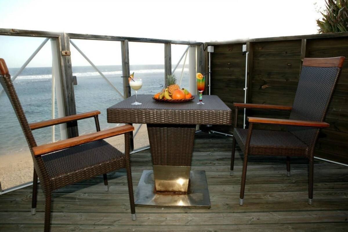 Um deck de madeira com uma mesa e duas cadeiras de vime, com vista para o oceano.