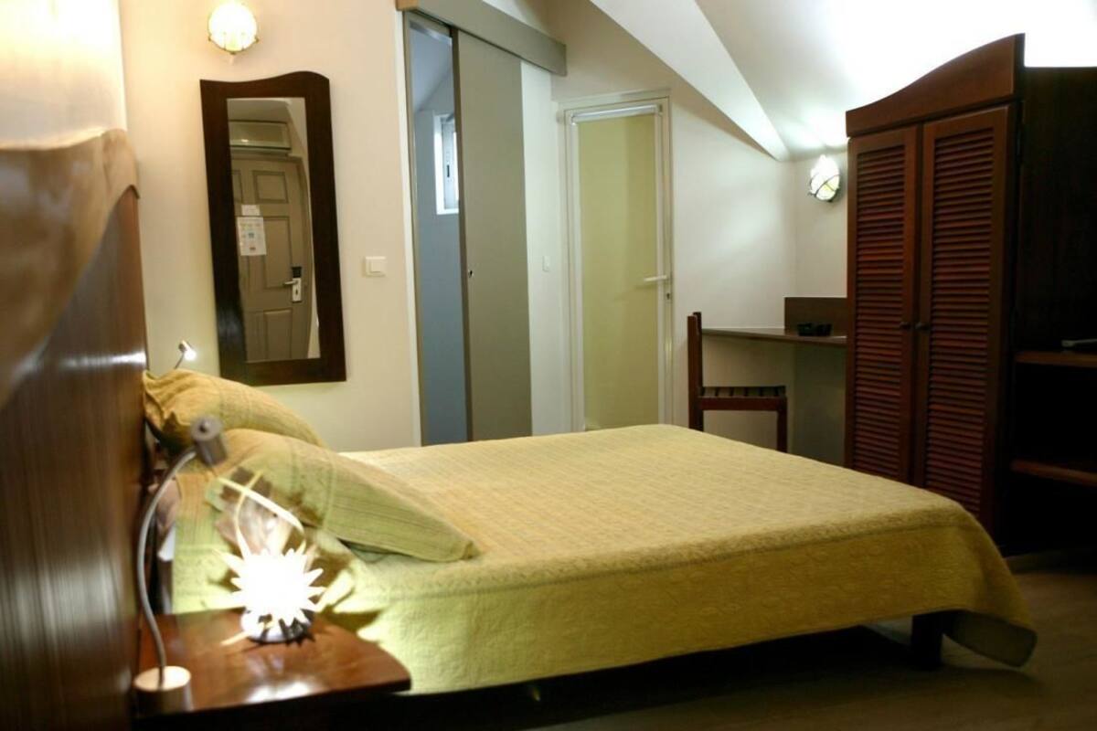 Um quarto com uma cama, uma mesa de cabeceira com abajur, um guarda-roupa e um espelho na parede.