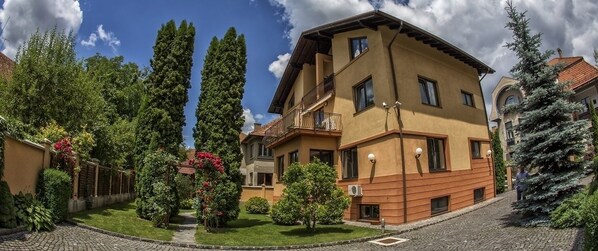A multi-story residential building with a balcony, surrounded by well-maintained gardens and trees.