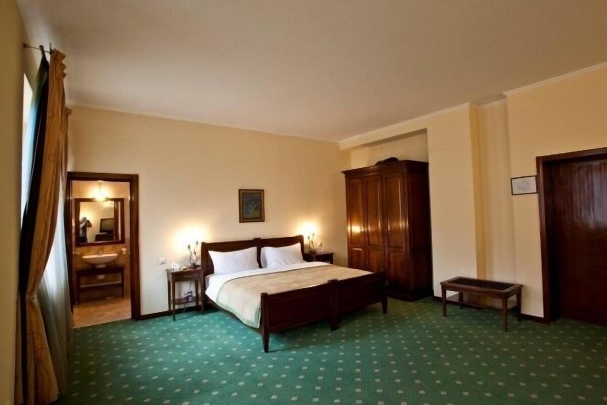 Een hotelkamer met een bed, een kledingkast, een nachtkastje, een spiegel en een groen tapijt met dessin.