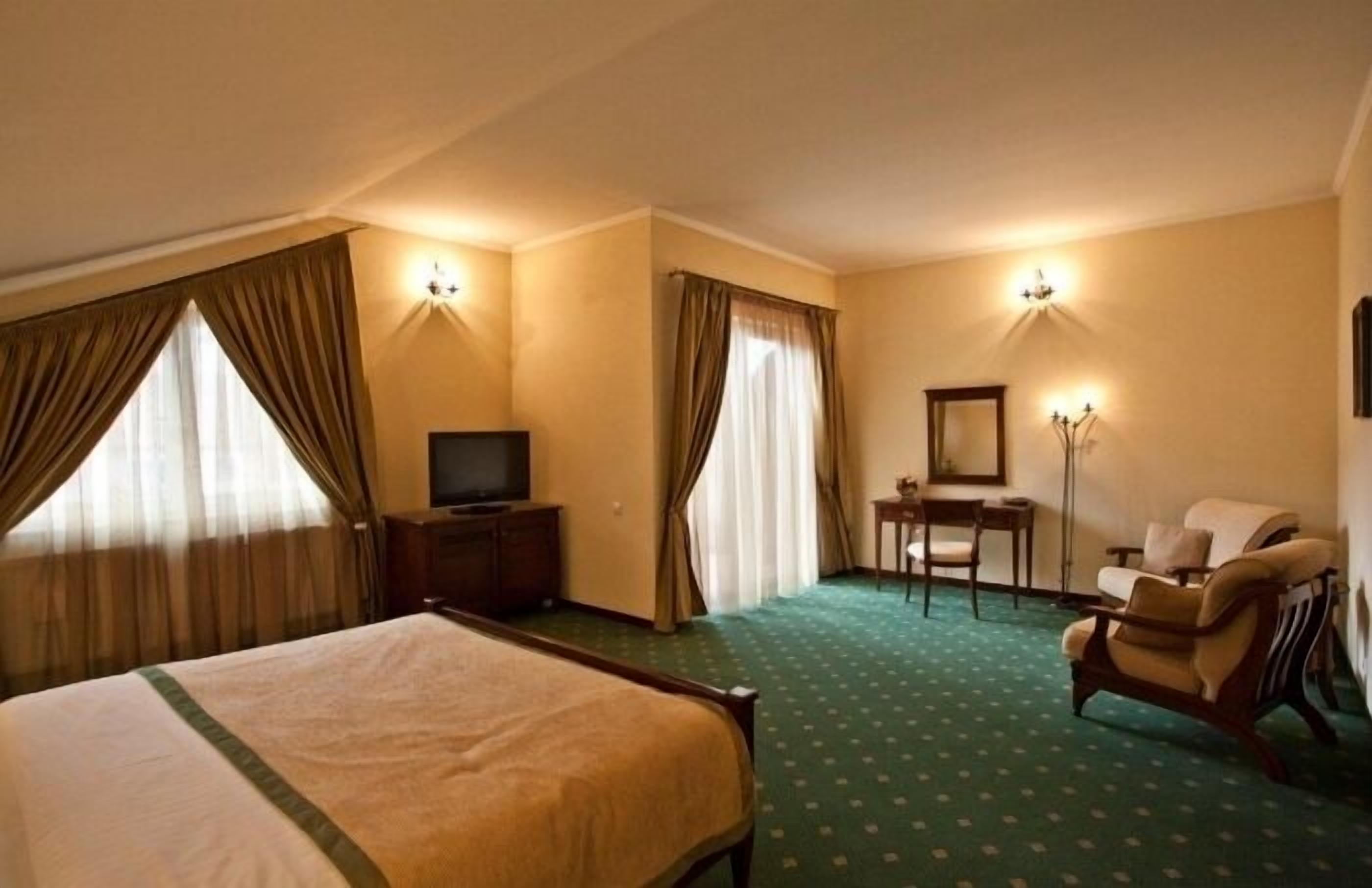 A hotel room with a large bed, a desk with a chair, a television, and two wall-mounted lamps.