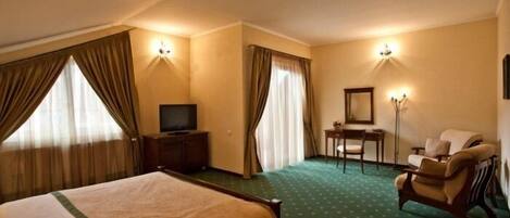 A hotel room with a large bed, a desk with a chair, a television, and two wall-mounted lamps.