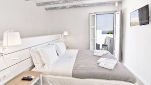 A hotel room with a bed, a nightstand, a lamp, a TV, and a balcony with a view. - Lindos Comfy Suites (Rhodes)