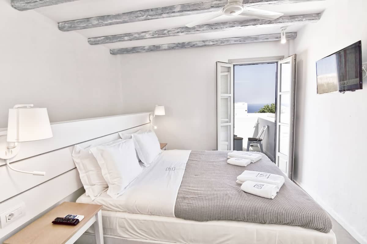 A hotel room with a bed, a nightstand, a lamp, a TV, and a balcony with a view.