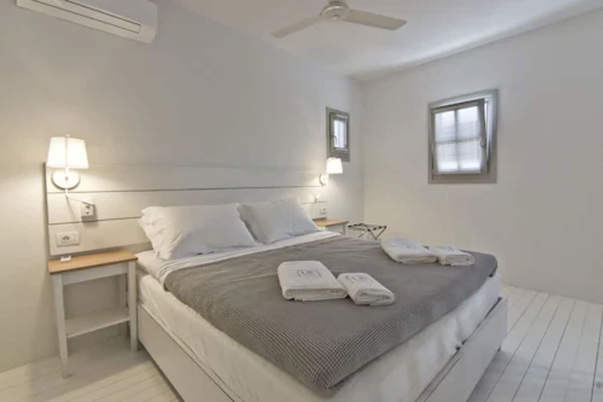 A bedroom with a bed, nightstands, a ceiling fan, and two windows.