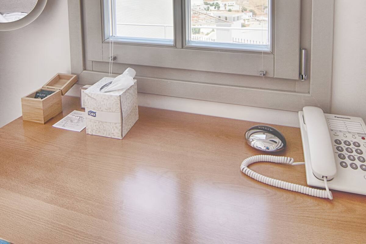A room with a wooden desk, a telephone, a tissue box, and a tissue box with tissues.