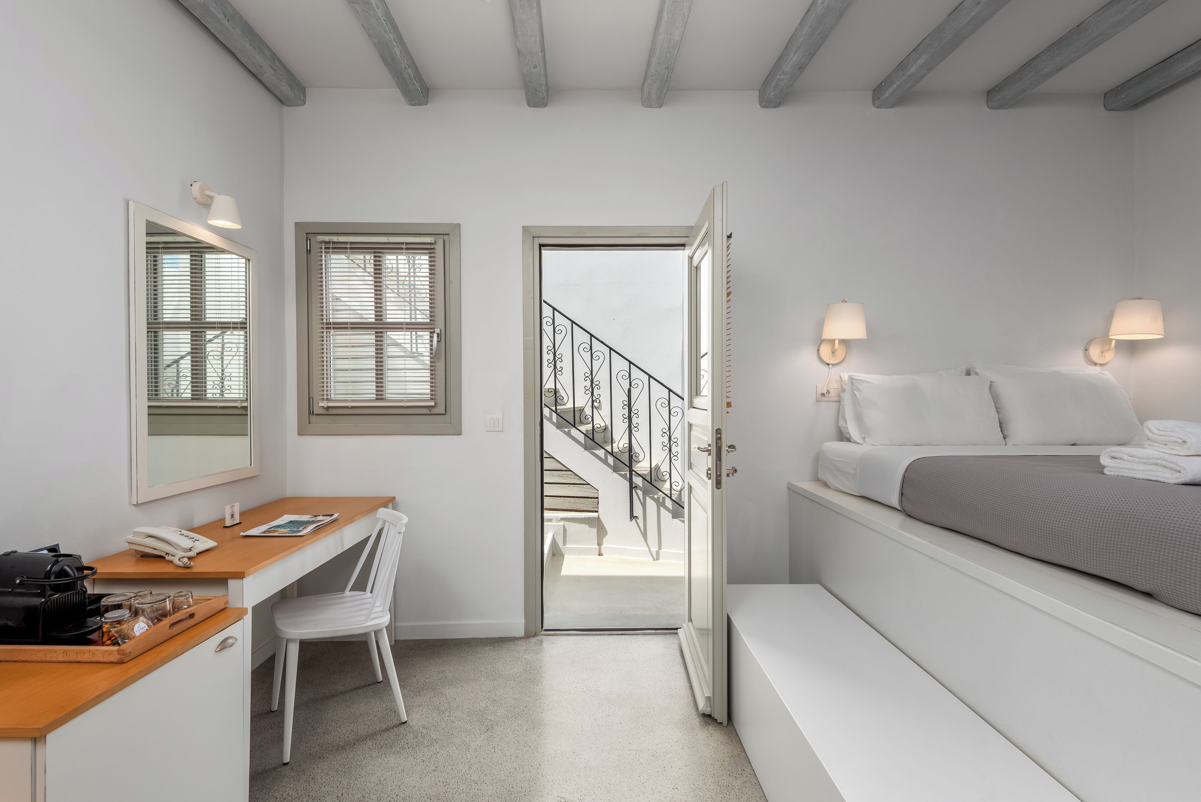 Un dormitorio con cama, lámparas de noche, un escritorio con silla, una ventana y una escalera que conduce al piso superior.