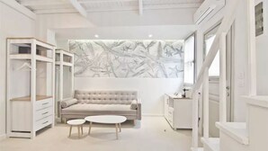 A modern, minimalist room with a tufted sofa, a small round table, and built-in shelving units. - Lindos Comfy Suites (Rhodes)