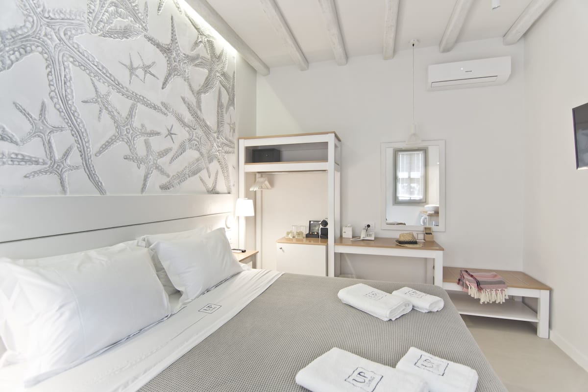 A hotel room with a bed, a desk, a mirror, and a wardrobe.