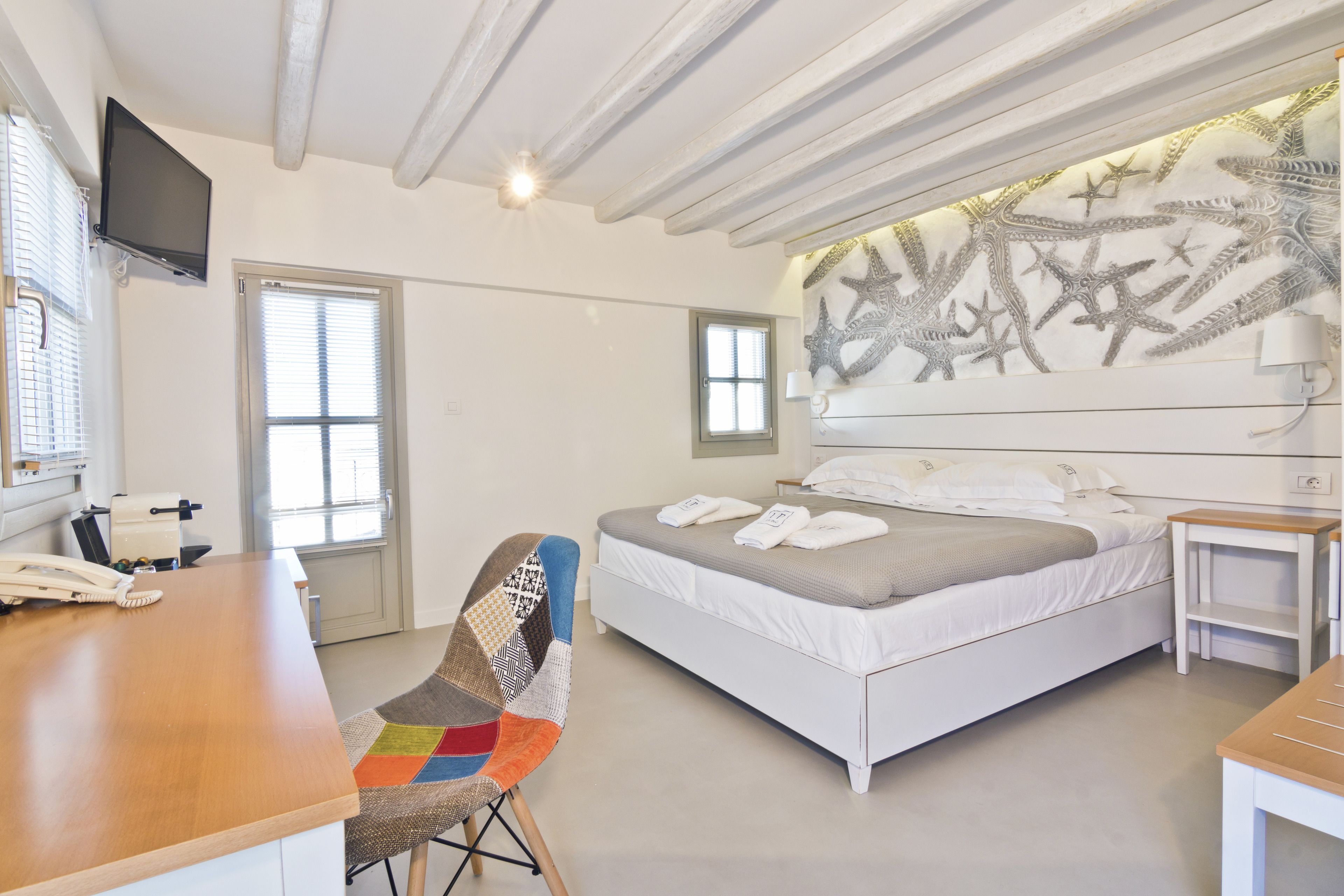 A bedroom with a bed, a desk, a chair, a TV, and a wall with starfish artwork.