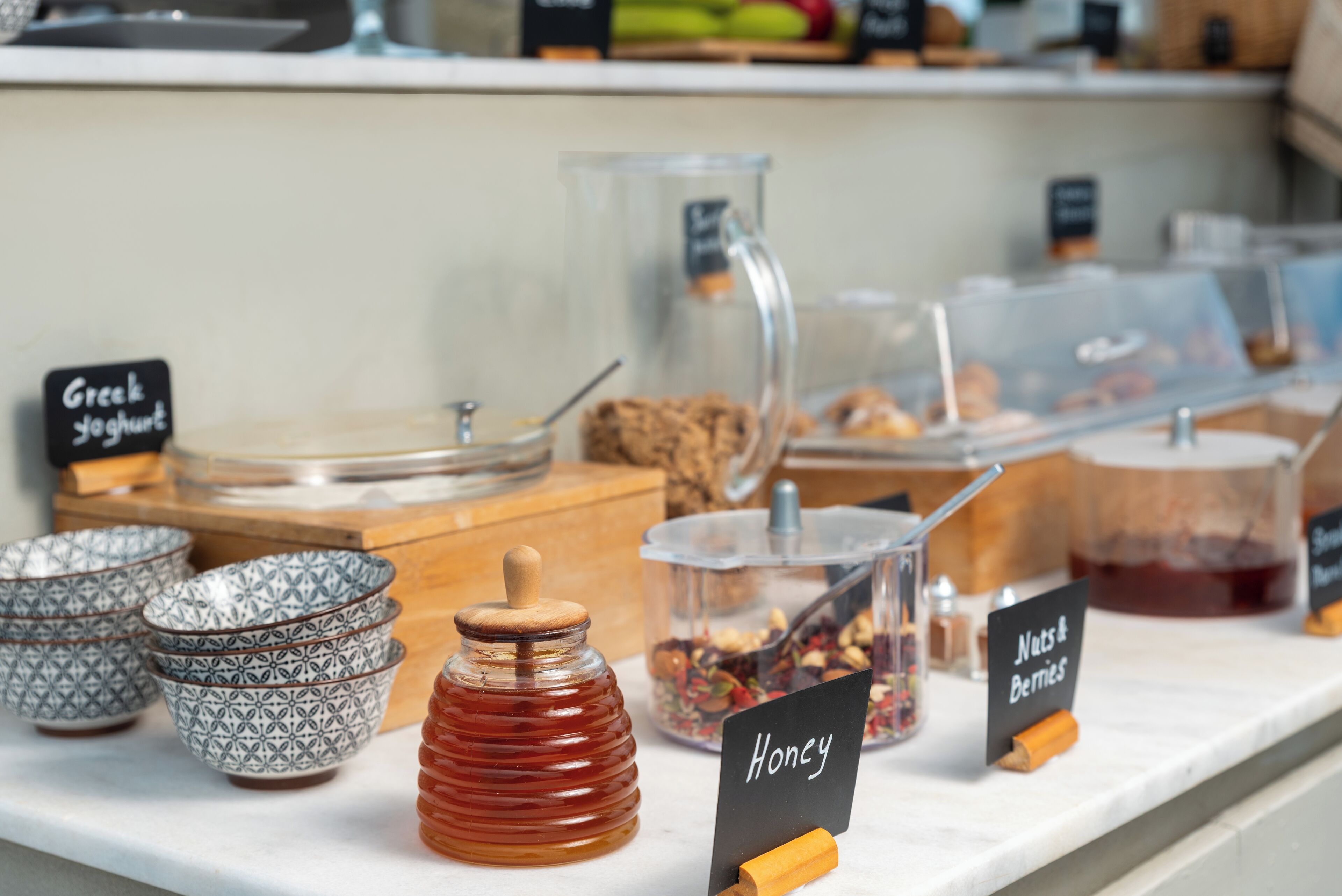 A breakfast bar with labeled containers of Greek yogurt, honey, nuts, and berries.