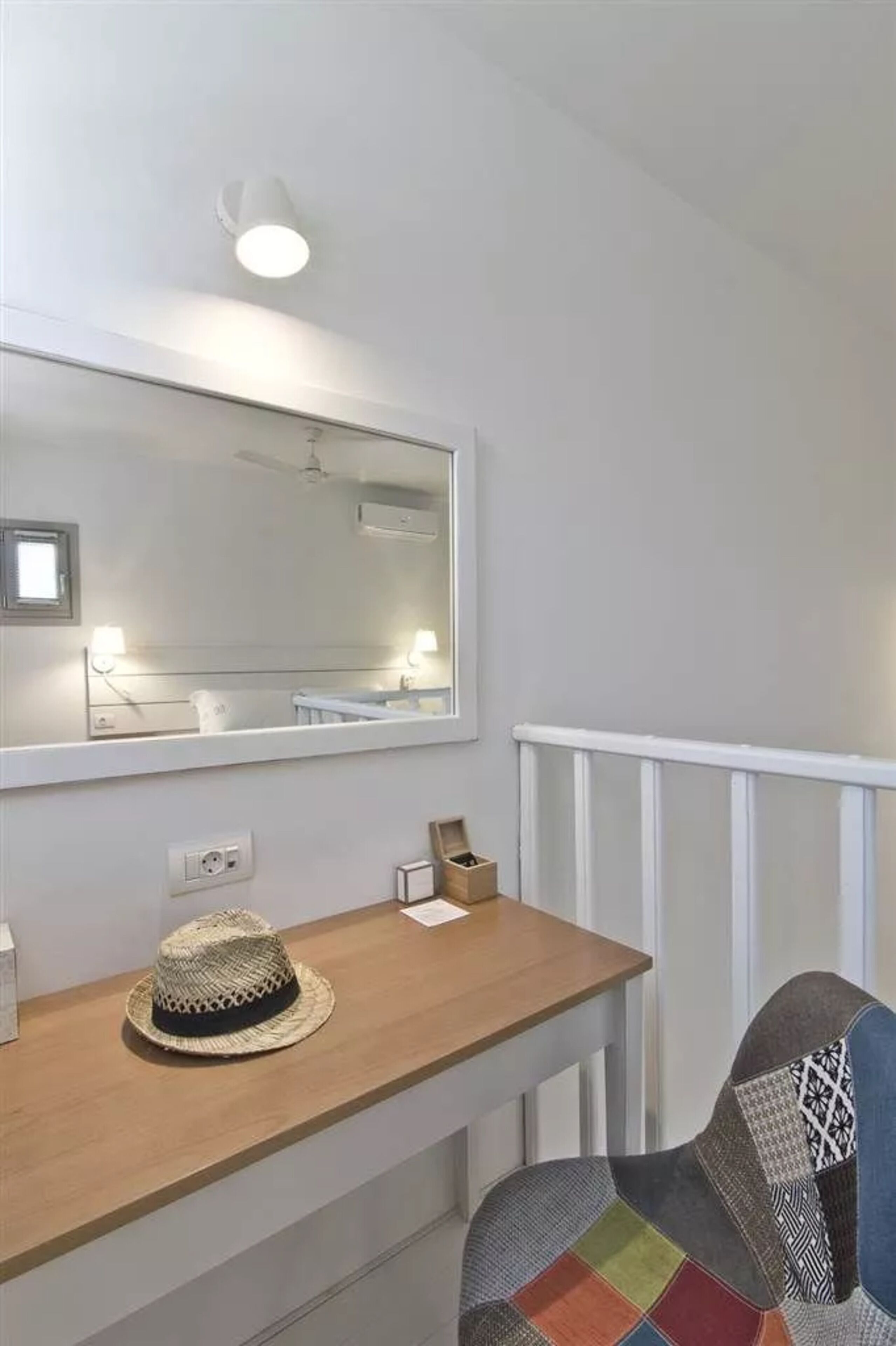 A room with a wooden desk, a mirror, a hat, and a patterned chair.