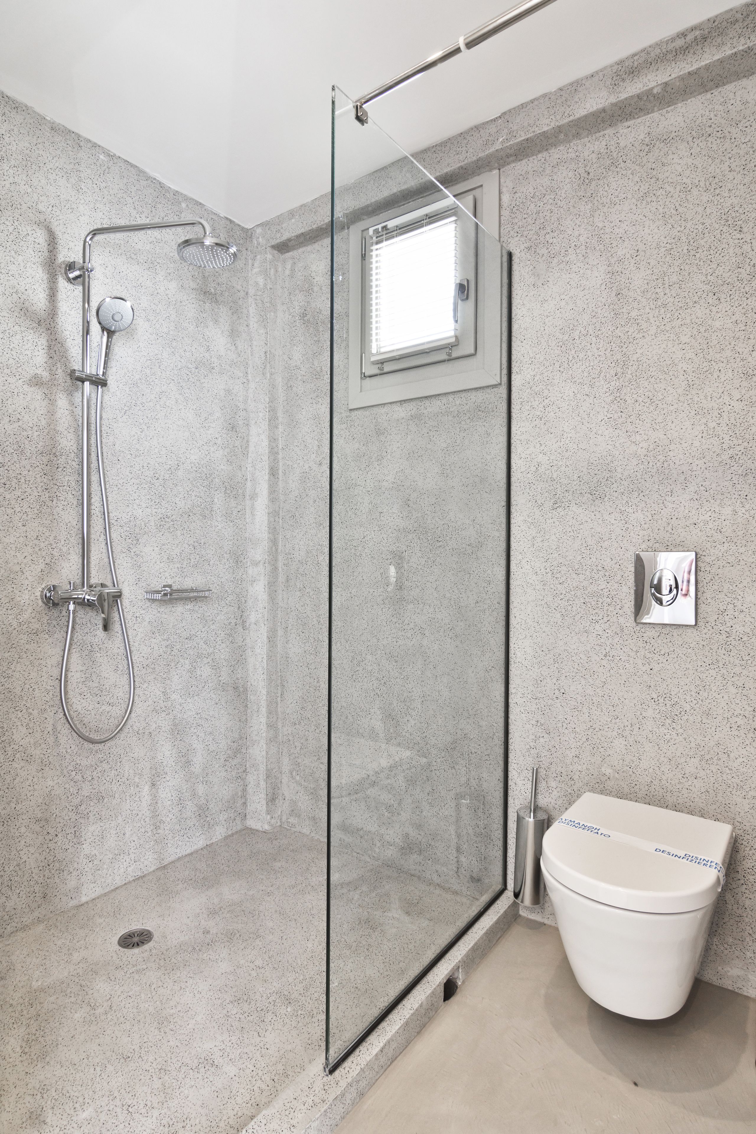 Ein modernes Badezimmer mit einer gläsernen Duschkabine, einer Toilette und einem kleinen Fenster.