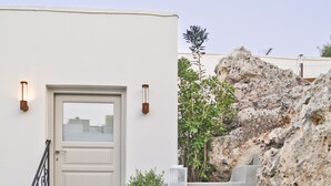 A set of concrete stairs leading to a white door with a glass panel, flanked by two wall-mounted light fixtures and small potted plants. - Lindos Comfy Suites (Rhodes)