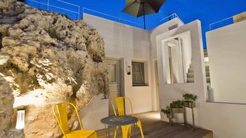 A modern outdoor seating area with a wooden deck, a stone wall, and a door leading to an interior space.