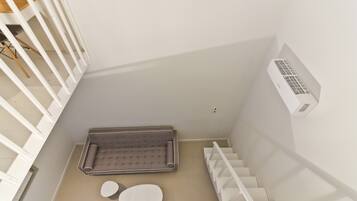 Uma escadaria moderna e minimalista com corrimão branco, uma pequena área de estar com um banco acolchoado e uma mesa redonda, e um ar condicionado fixado na parede.