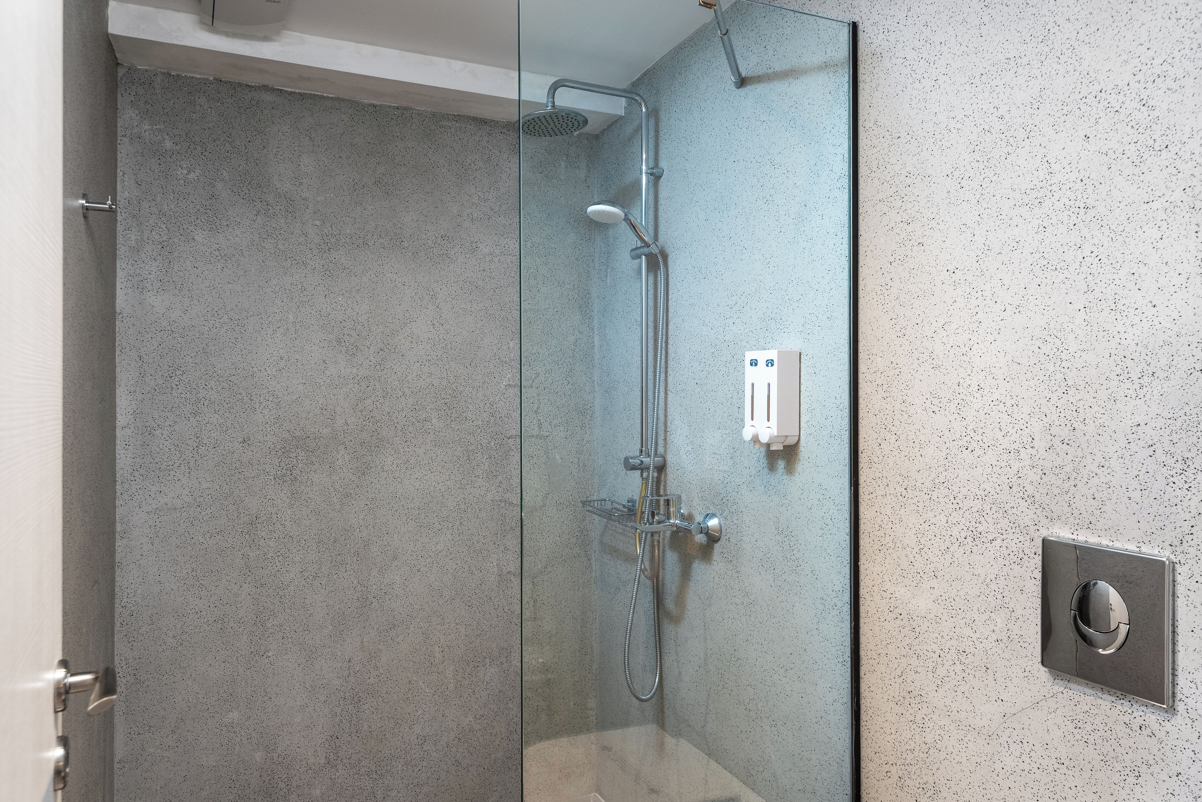 A glass-enclosed shower with a handheld showerhead and a wall-mounted control panel.