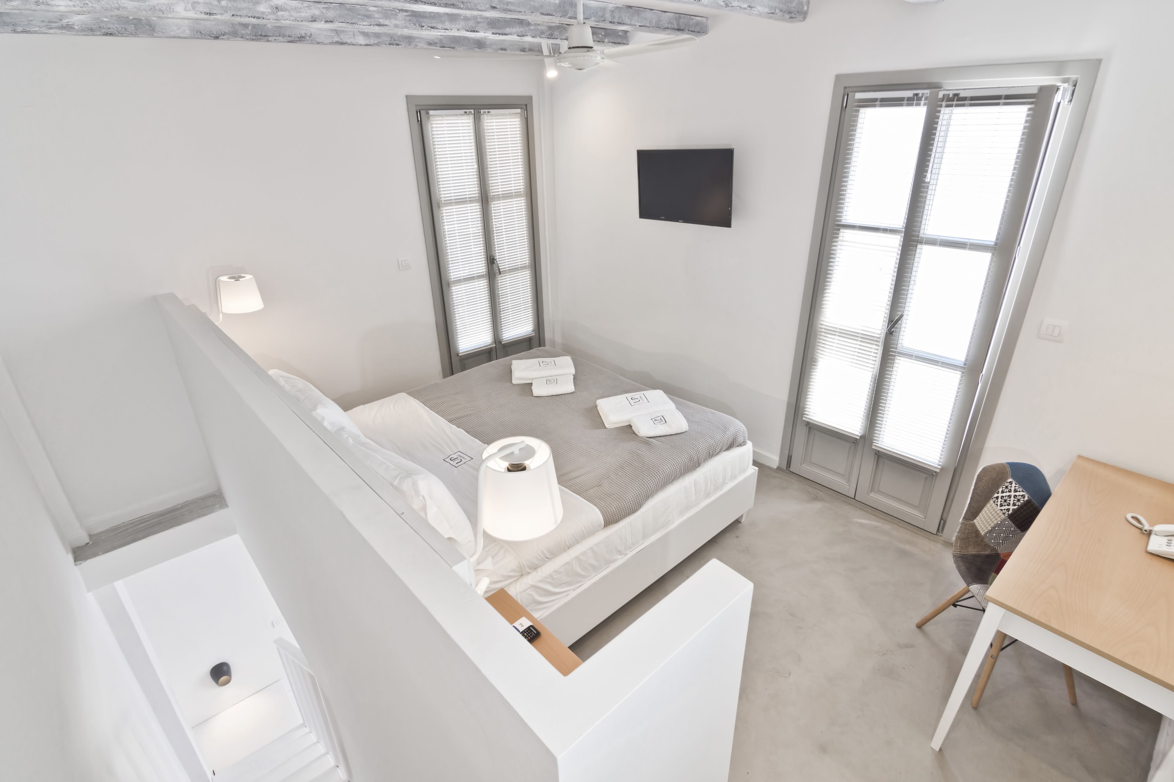 A modern, well-lit bedroom with a bed, bedside lamps, and a desk.