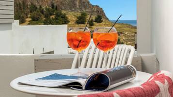 Un balcón con dos sillas blancas, una mesa con una revista y dos vasos de jugo de naranja.