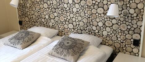 A double bed with two decorative pillows, a bedside table with a lamp, and a wall with a circular wood pattern.