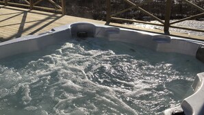 Un bain à remous avec une terrasse en bois et une vue sur un lac et des collines en arrière-plan.