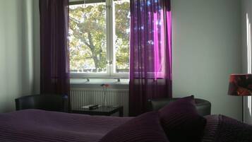 Une chambre à coucher avec un lit, une chaise, une table et une fenêtre avec des rideaux.