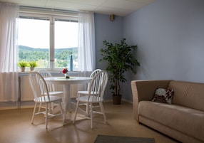 Quarto com uma mesa de jantar e cadeiras, um sofá, uma planta em vaso e vista para o exterior.