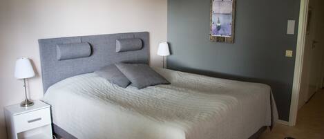 Un letto rifatto con cura, con una testiera grigia, un comodino con una lampada e un quadro appeso alla parete.