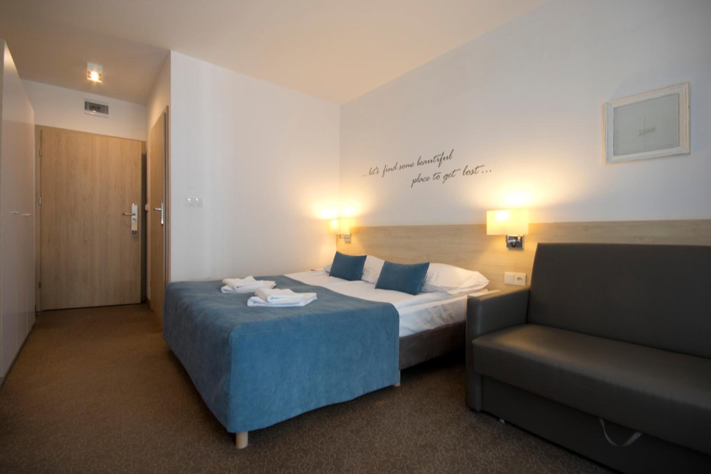 A hotel room with a bed, a sofa, and a wall with a motivational quote.