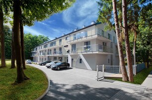 Un edificio residencial de varios pisos con balcones, un camino pavimentado y automóviles estacionados.