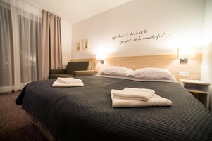 Una habitación de hotel con una cama grande, dos mesitas de noche, un cabecero y una cita en la pared.