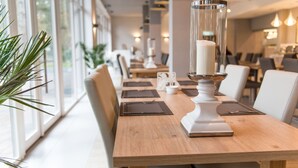 Un comedor con una mesa de madera dispuesta para dos personas, un centro de mesa con velas y vistas al exterior a través de amplios ventanales.