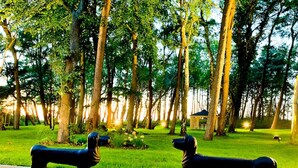 Un parque con dos estatuas de perros negros sobre un sendero pavimentado, rodeado de árboles y un pabellón al fondo.