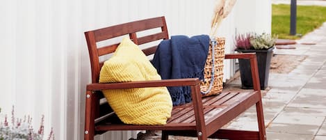 A wooden bench with cushions against a white wall, a potted plant, and a lamp post.