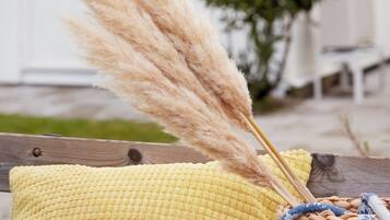 Una cesta de mimbre con plumas de plumerillo y un cojín amarillo sobre una terraza de madera.