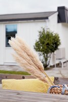 Una cesta de mimbre con plumas de plumerillo y un cojín amarillo sobre una terraza de madera.